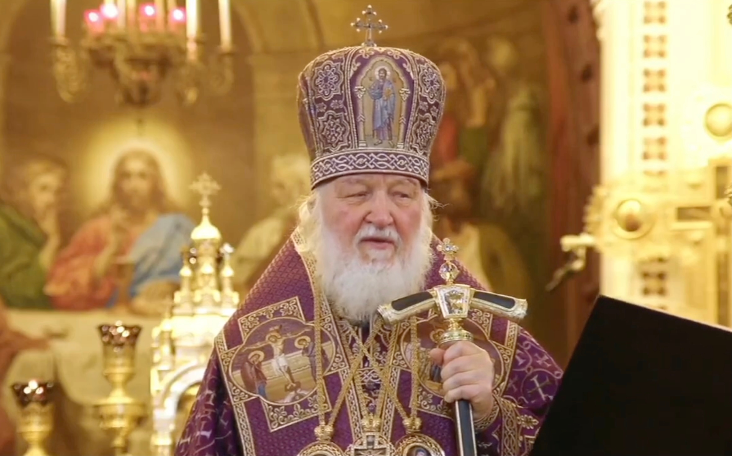 Патриарх Кирилл заглядывает в поднесенную ему папку во время проповеди