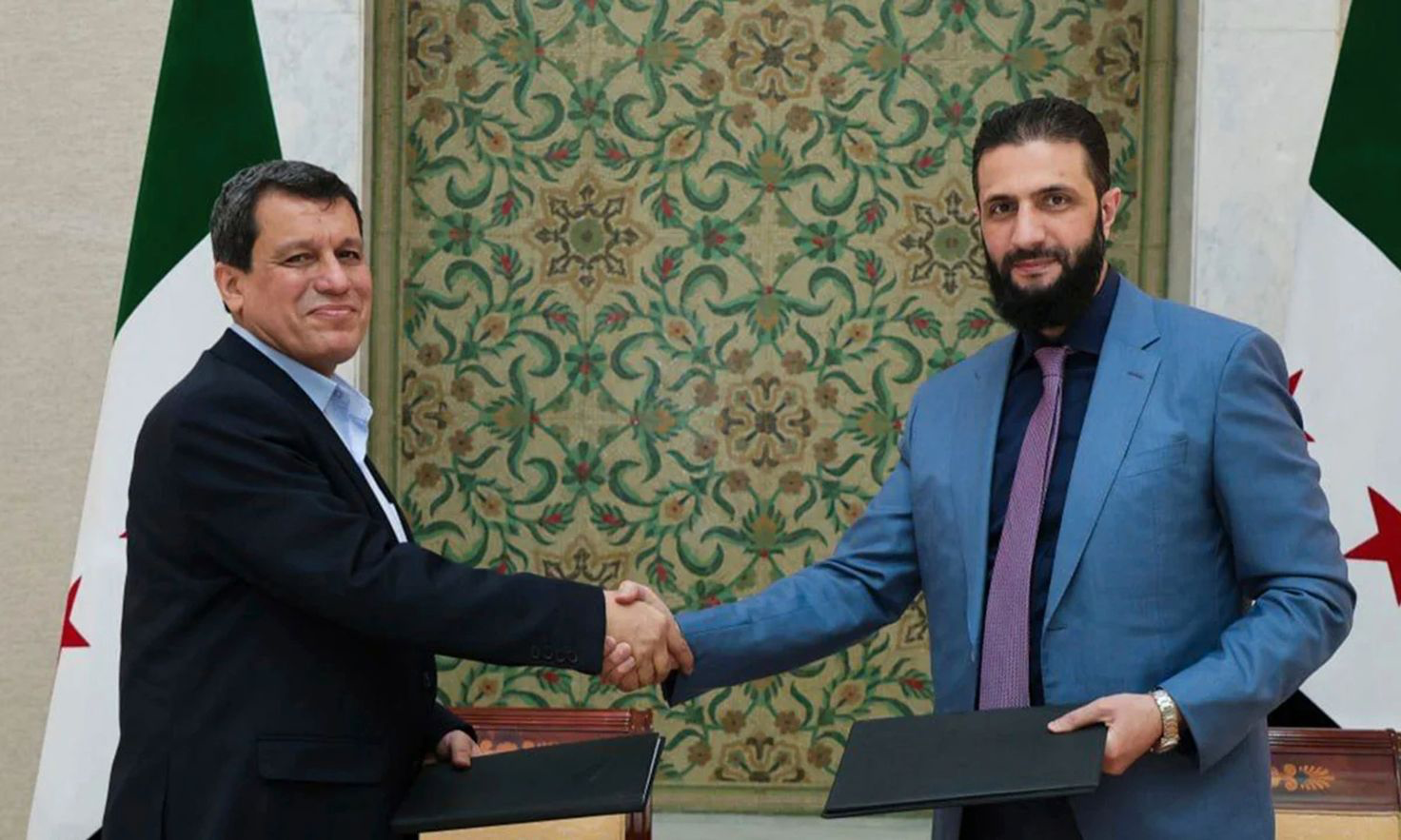 Interim Syrian President Ahmed al-Sharaa, right, shakes hands with Mazloum Abdi, commander of the Kurdish-led Syrian Democratic Forces in Damascus following the signing of an integration agreement.